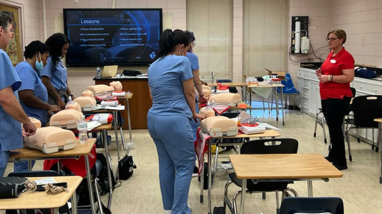 a friendly nurse instructor calmly coaching an adult student during CPR skills verification, Lafayette Louisiana, Cajun South Louisiana feel, professional training classroom, mannequins and AED trainers visible